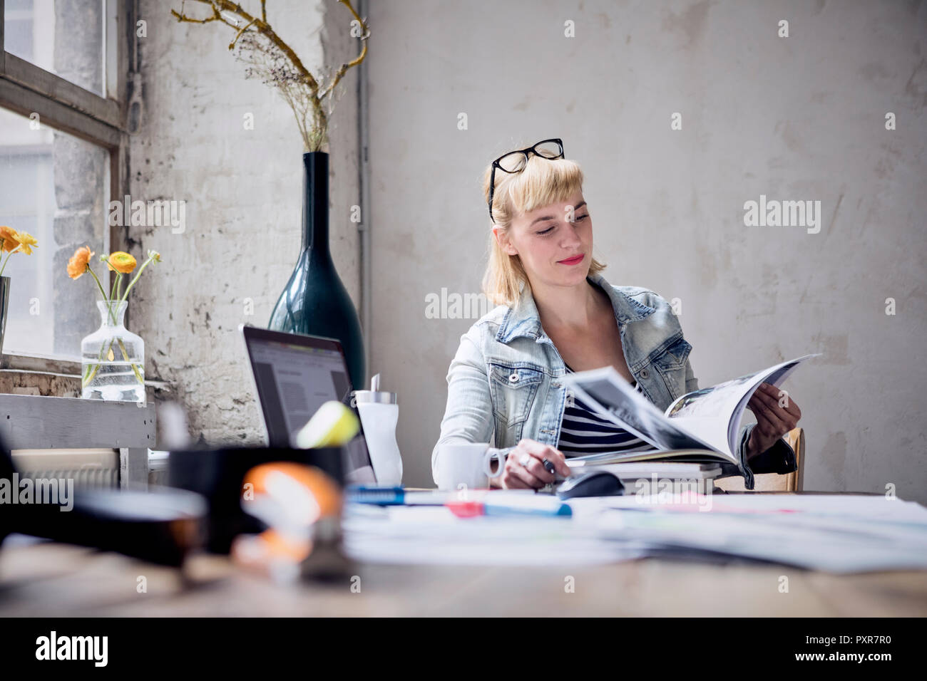 Ritratto di donna sorridente seduto alla scrivania in un loft sfogliando prenota Foto Stock