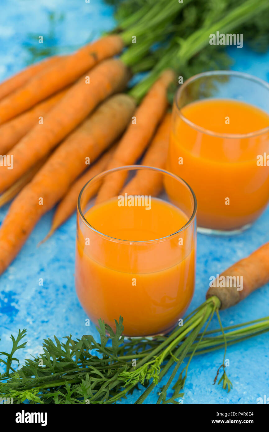Due bicchieri di fresco succo di carota e carote sulla luce di massa blu Foto Stock
