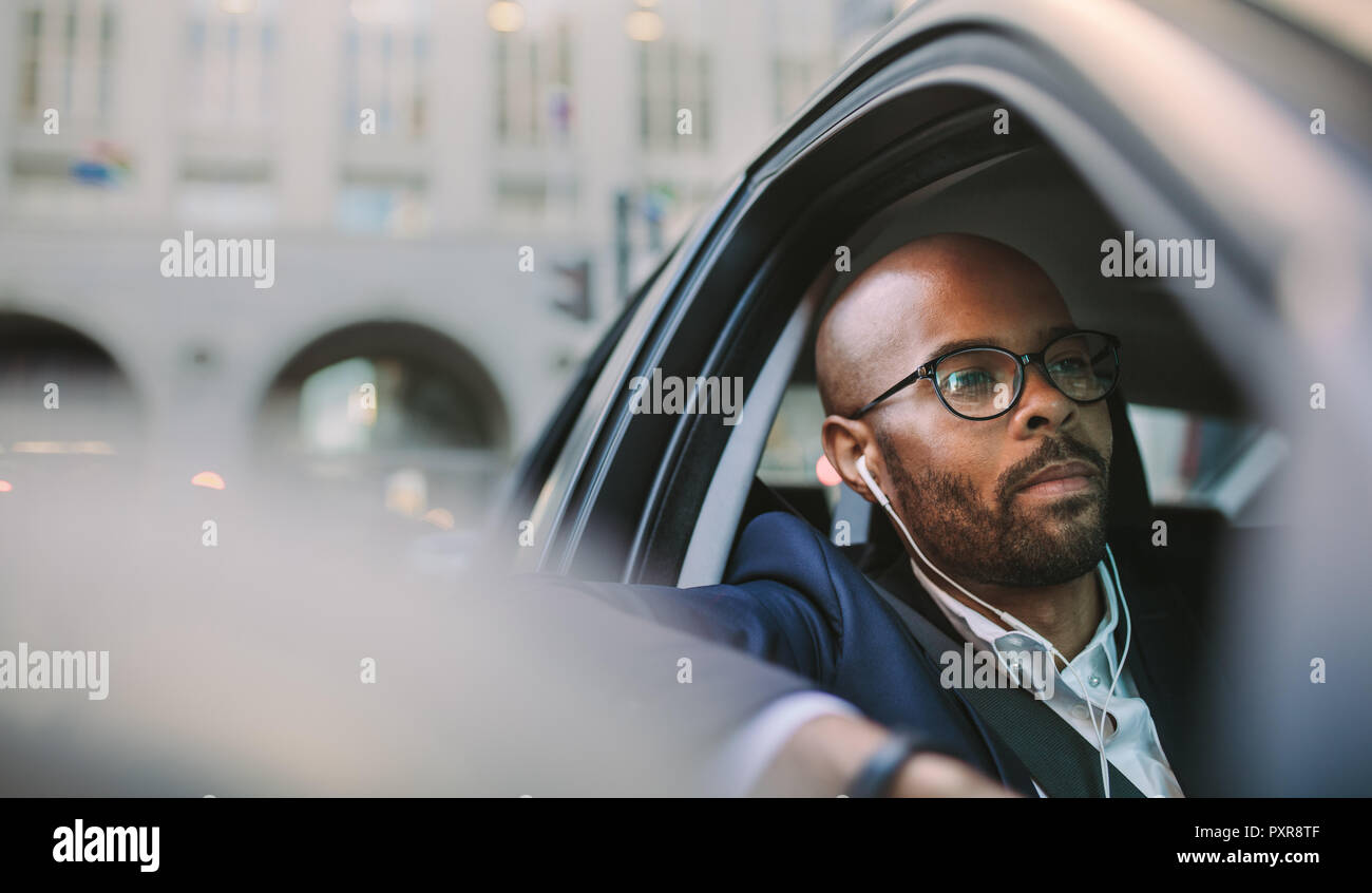 Imprenditore che indossa gli auricolari e ascolto mcon durante la guida di un'auto. Imprenditore africano essendo bloccato nel traffico di mattina. Foto Stock
