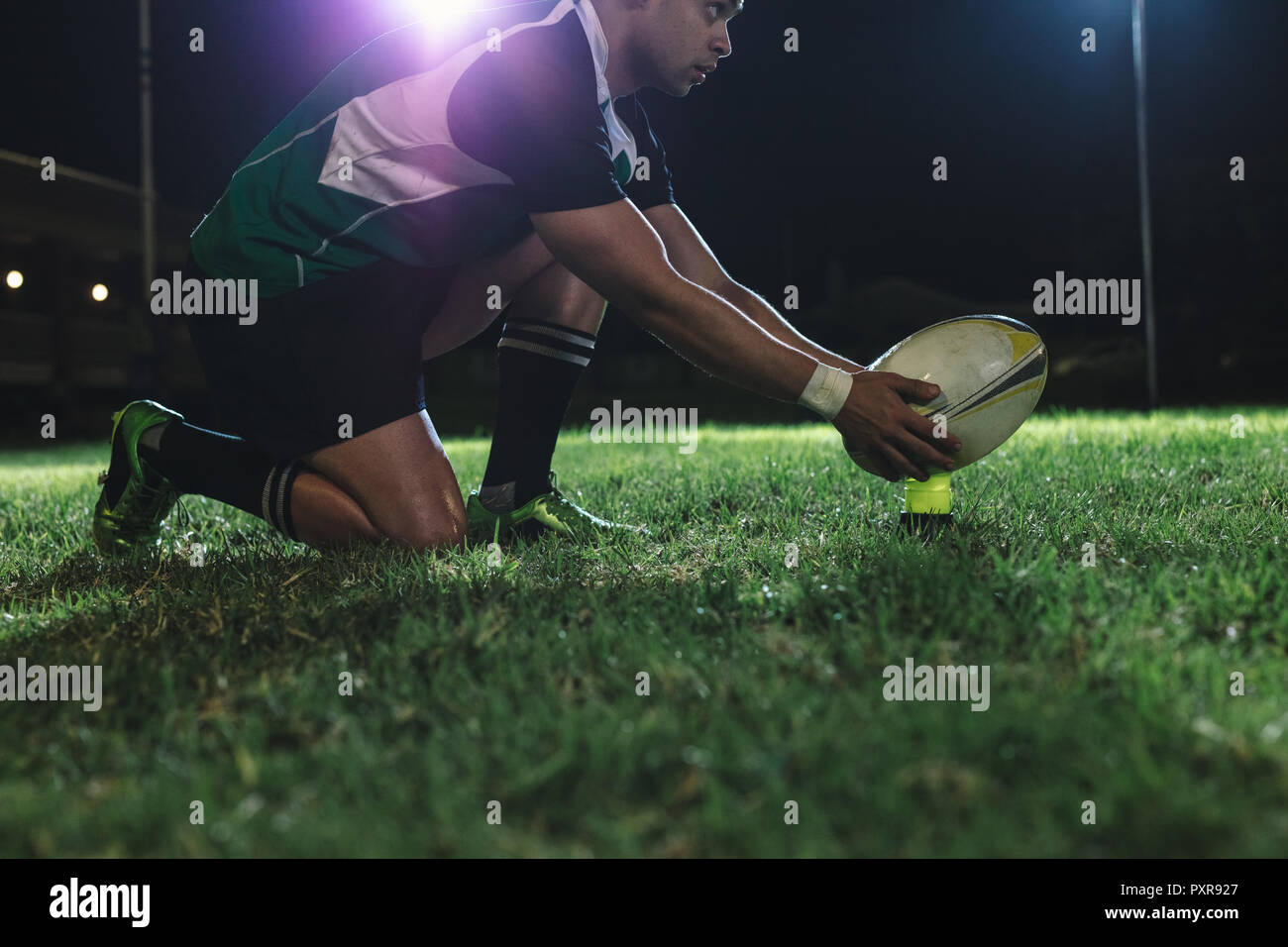 giocatore di rugby che mette la palla sul tee per il tiro di rigore durante la partita. giocatore di rugby che fa un tiro di rigore sotto le luci nell'arena sportiva. Foto Stock
