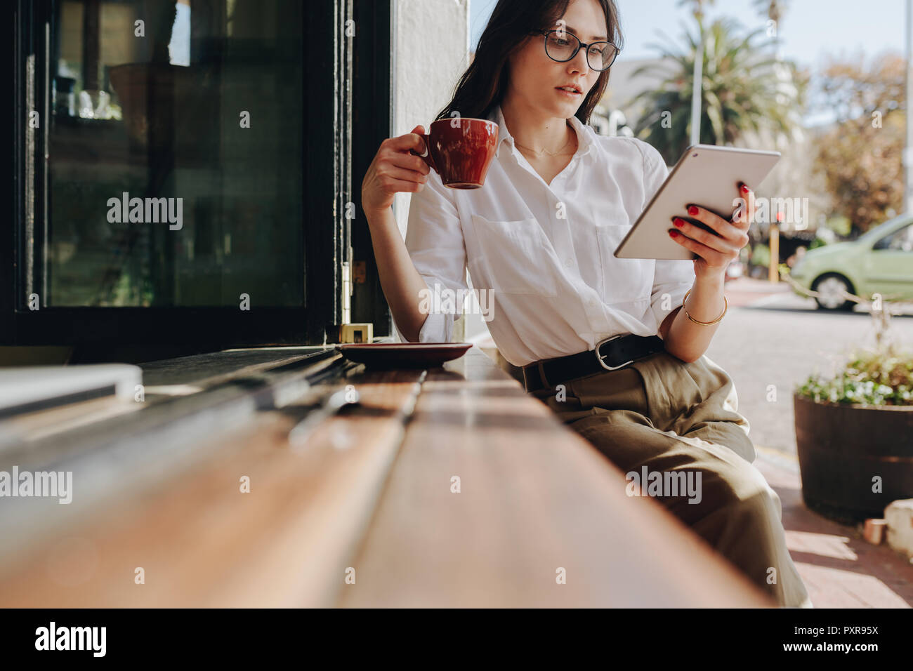 Imprenditrice donna che si rilassa al bar, bevendo un caffè e leggendo e-mail sul suo tablet digitale. donna d'affari che usa un tablet digitale e beve cof Foto Stock