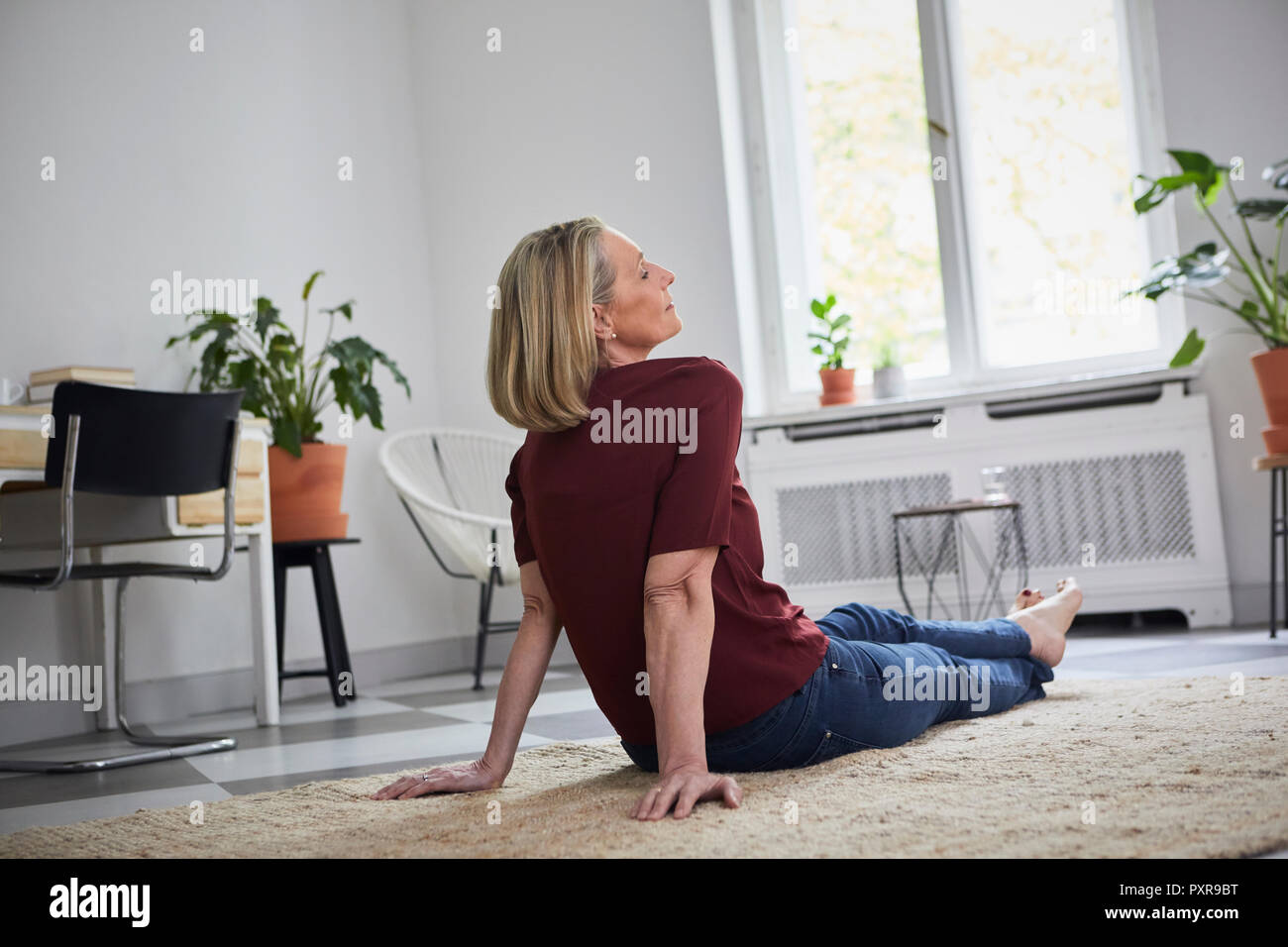 Rilassata donna matura seduta sul pavimento a casa Foto Stock