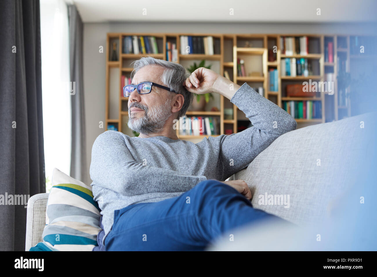 Uomo maturo rilassante sul lettino a casa guardando fuori della finestra Foto Stock