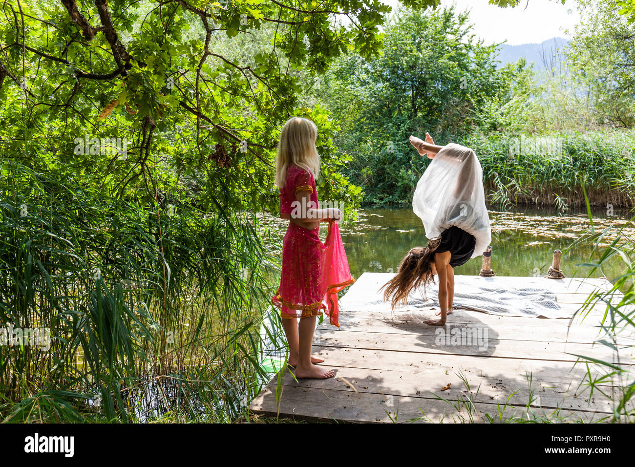 Ragazza sul molo al laghetto guardando amico facendo un handstand Foto Stock