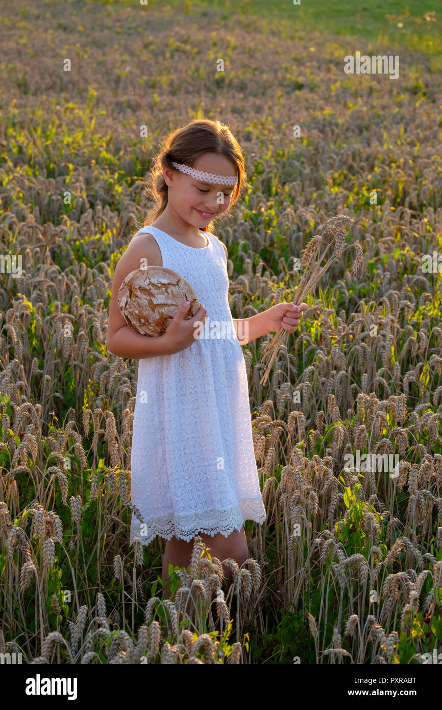Ragazza in piedi nel campo di grano, tenendo il pane fresco Foto Stock