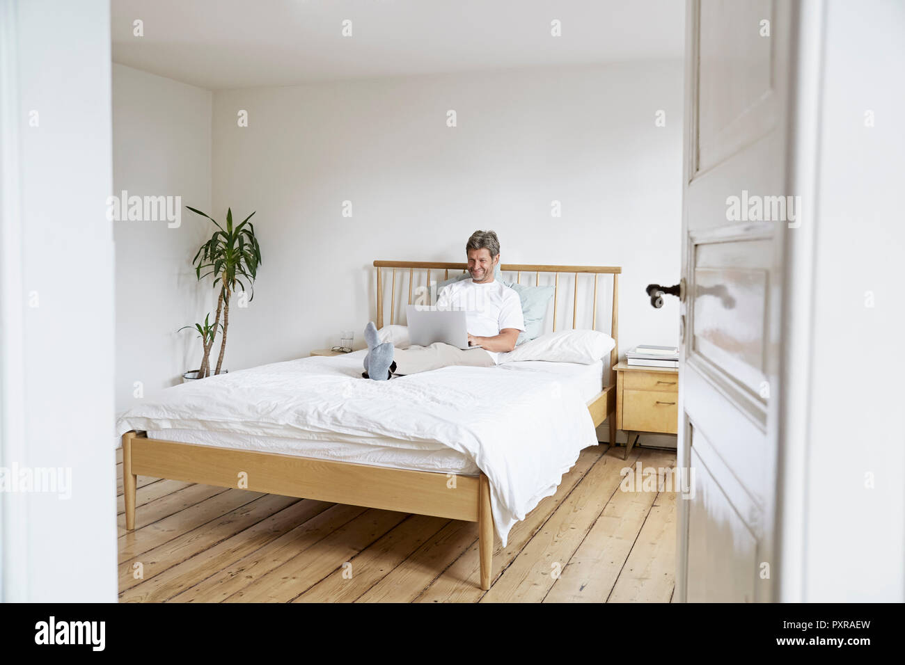 Uomo maturo rilassante con computer portatile in camera da letto Foto Stock