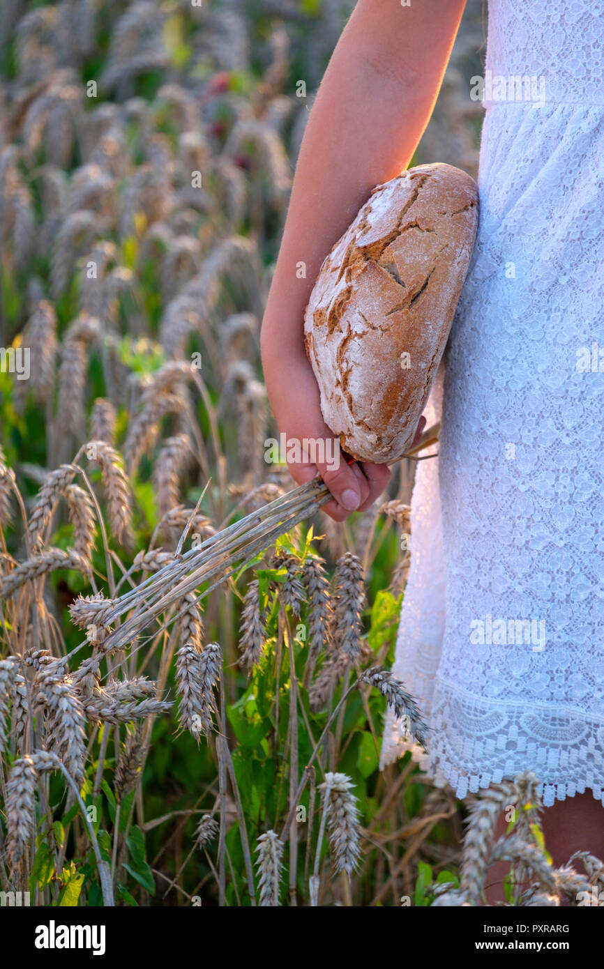 Ragazza in piedi nel campo di grano, tenendo il pane fresco Foto Stock