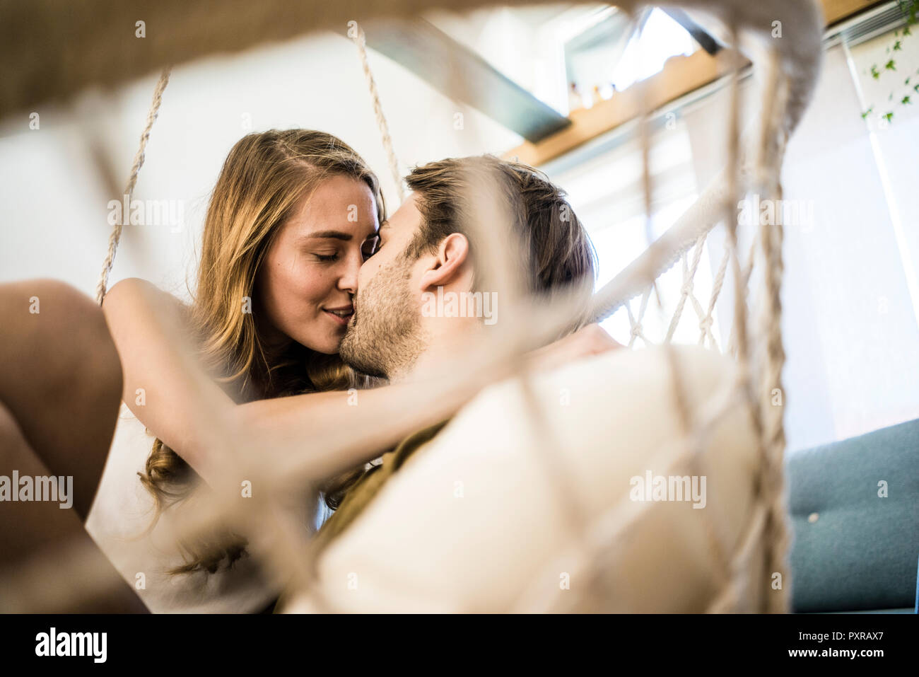 Felice coppia affettuoso bacio nella sedia pensili a casa Foto Stock