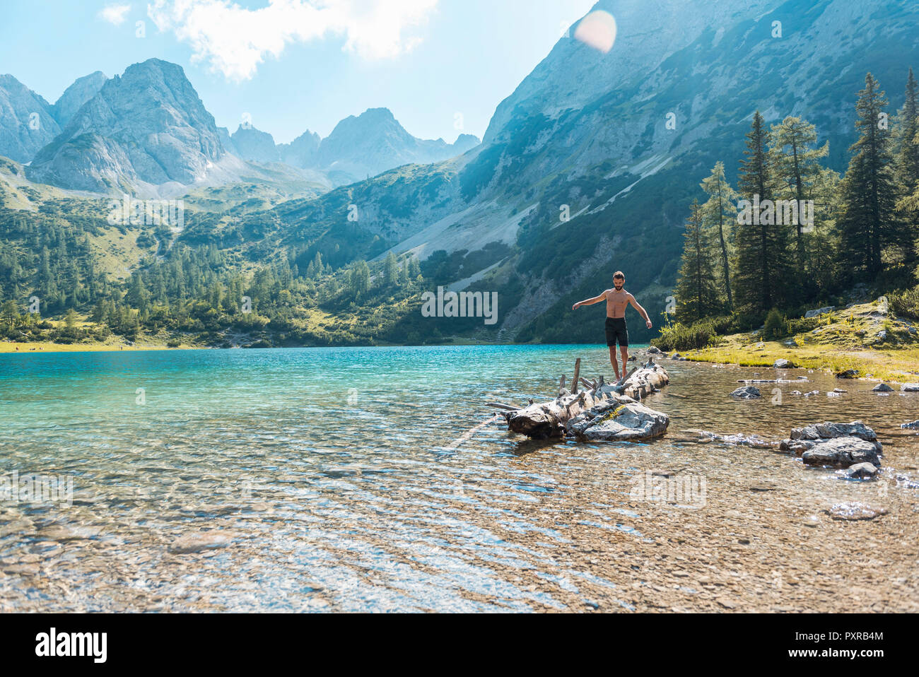 Austria, Tirolo, giovane uomo al Lago di bilanciamento Seebensee sul tronco di albero Foto Stock