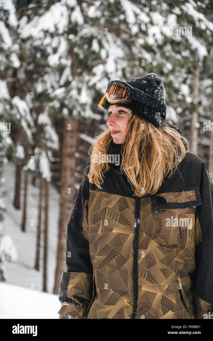 Giovane donna in skiwear in inverno foresta guardando lateralmente Foto Stock