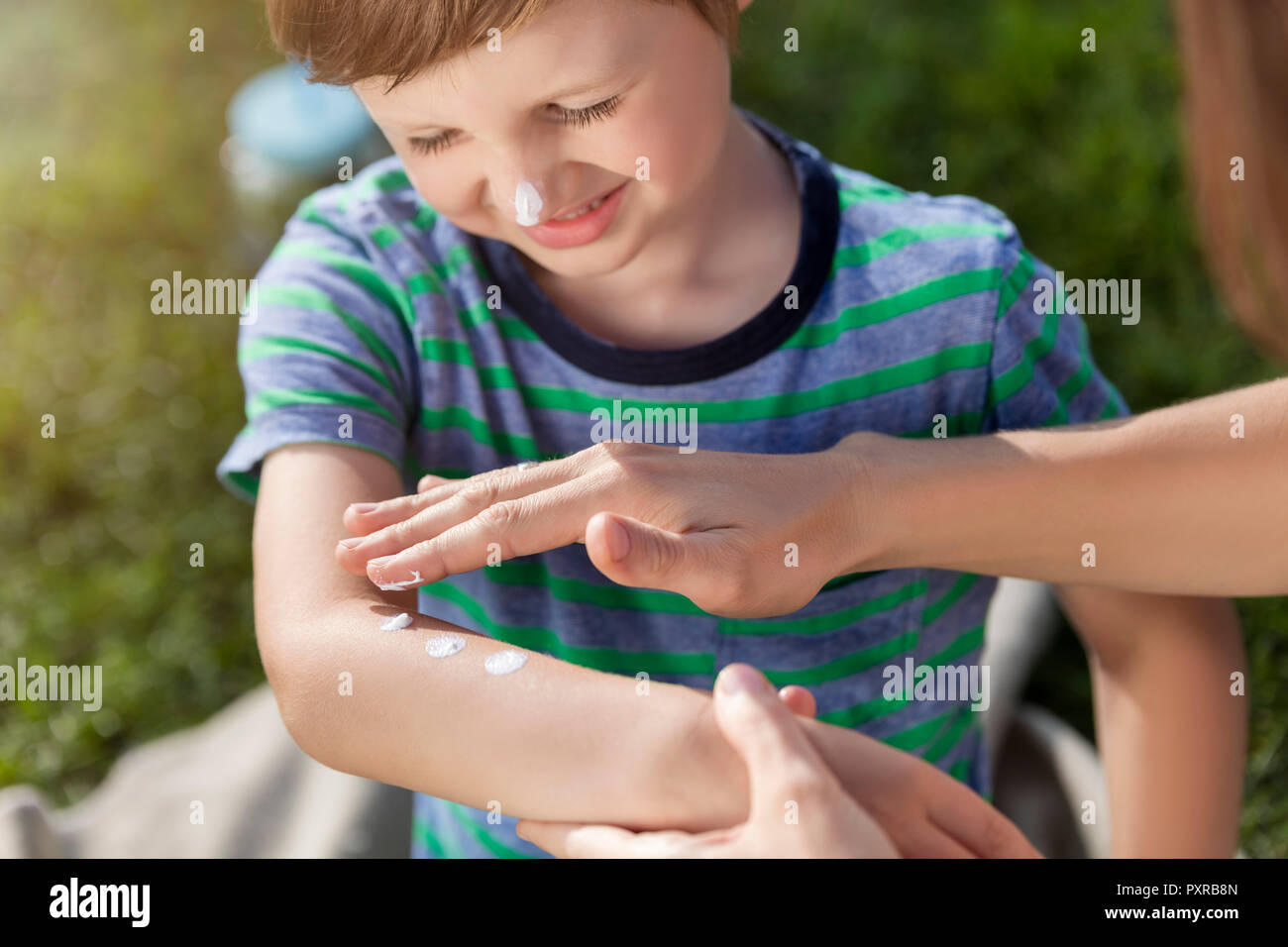 Madre di applicare la crema solare sul figlio del braccio Foto Stock
