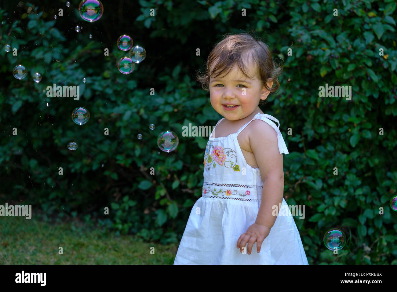 Ritratto di sorridente bambina con bolle di sapone in giardino Foto Stock
