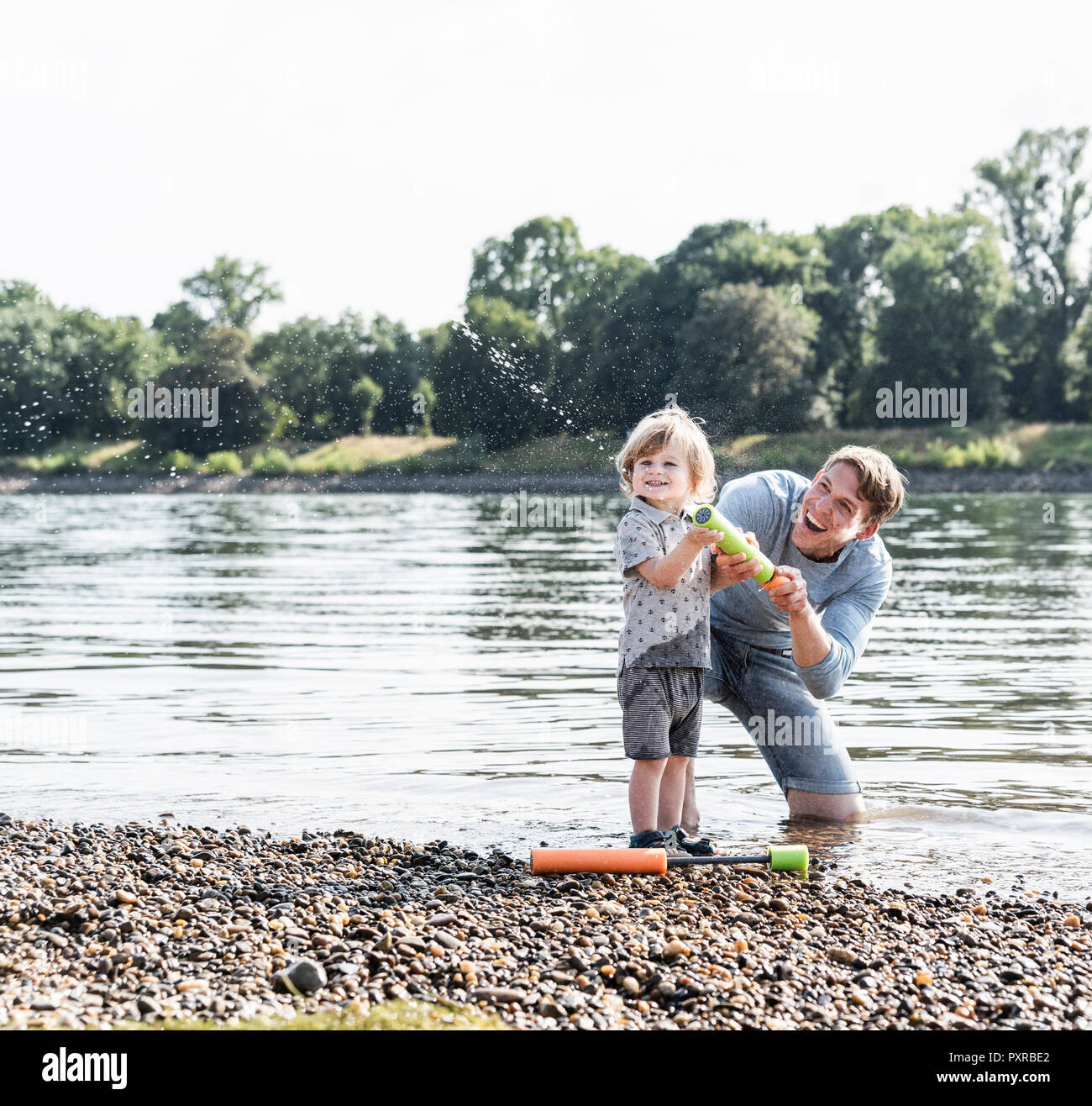 Padre e figlio divertendosi al Riverside, giocando con una pistola ad acqua Foto Stock