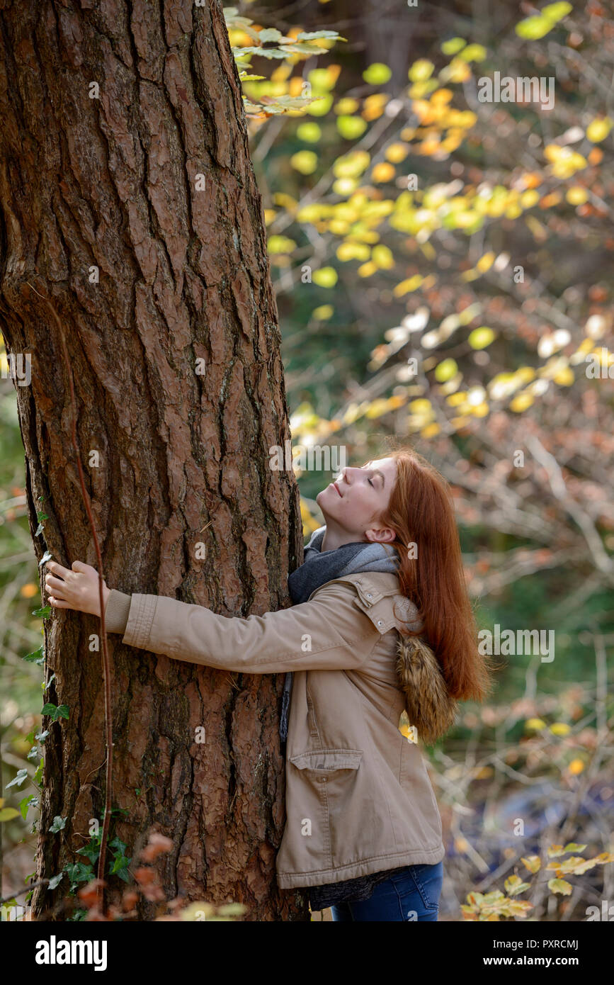 Sorridente ragazza adolescente abbracciando tronco di albero nella foresta autunnale Foto Stock