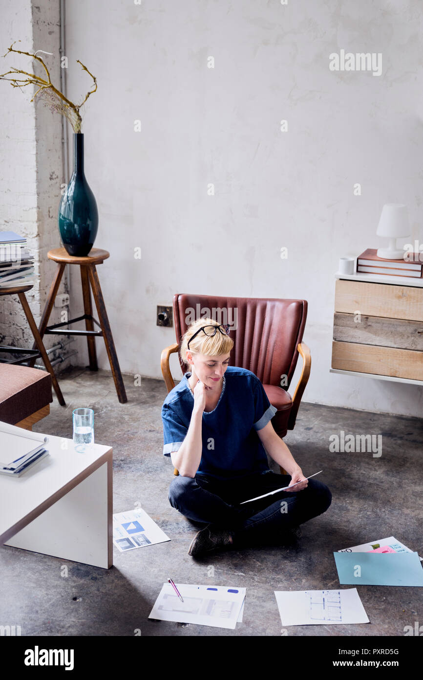 Donna seduta su floot in un loft guardando papers Foto Stock