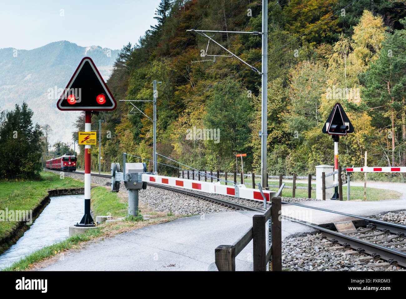 Railraod incrocio con lampeggiare le luci di avvertimento di rosso e un treno in avvicinamento in campagna svizzera Foto Stock