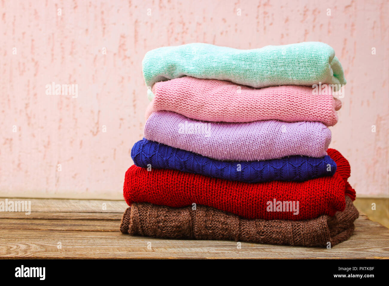 Pila di coloratissimi vestiti caldi su sfondo di legno. Foto Stock
