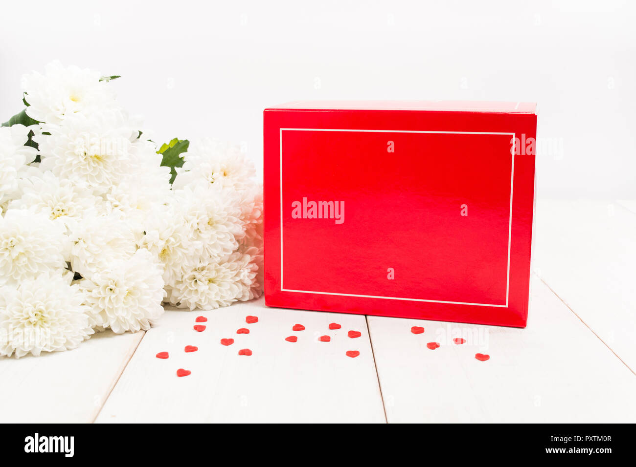 Confezione regalo rossa con copia spazio con fiori di colore bianco sul tavolo di legno e piccoli cuori dolci Foto Stock