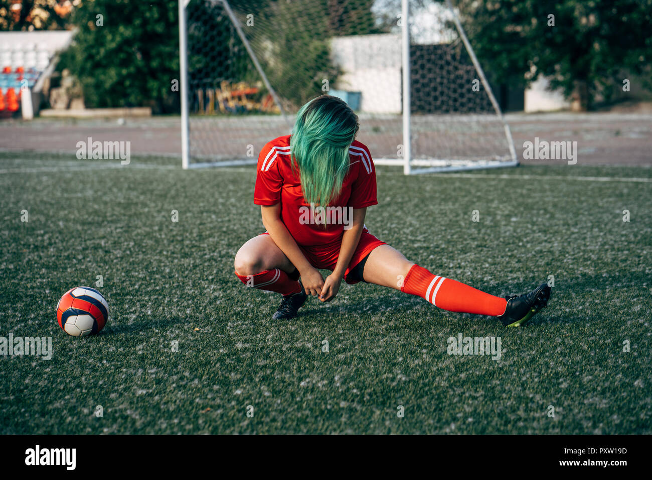 Giovane donna stretching sul terreno di calcio accanto alla sfera Foto Stock