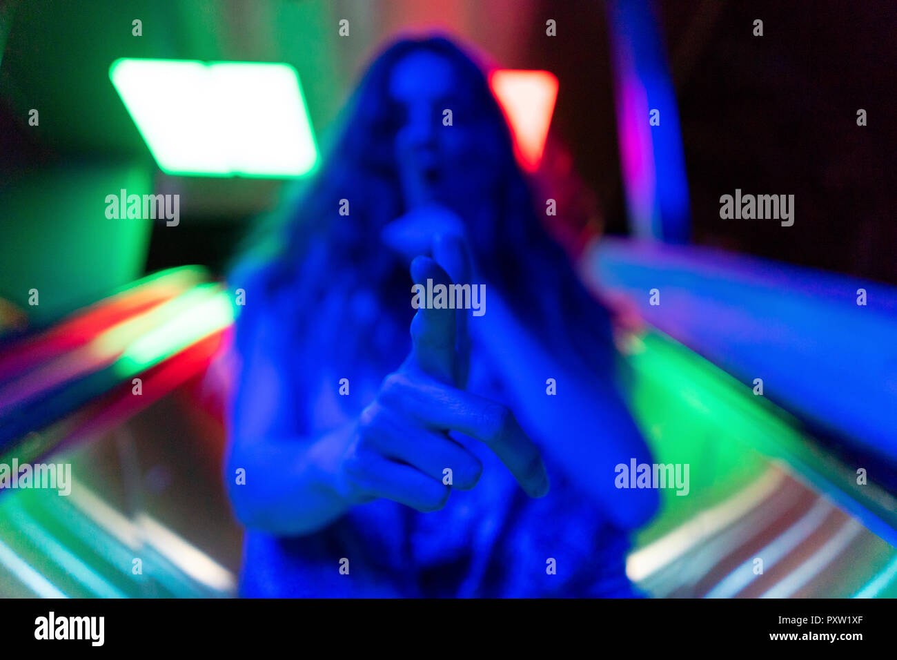 Illuminato blu giovane donna che fa il gesto di tiro con la sua mano, close-up Foto Stock