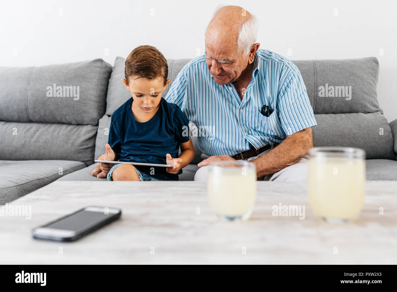 Nonno e nipote insieme seduti sul divano di casa guardando a tavoletta digitale Foto Stock