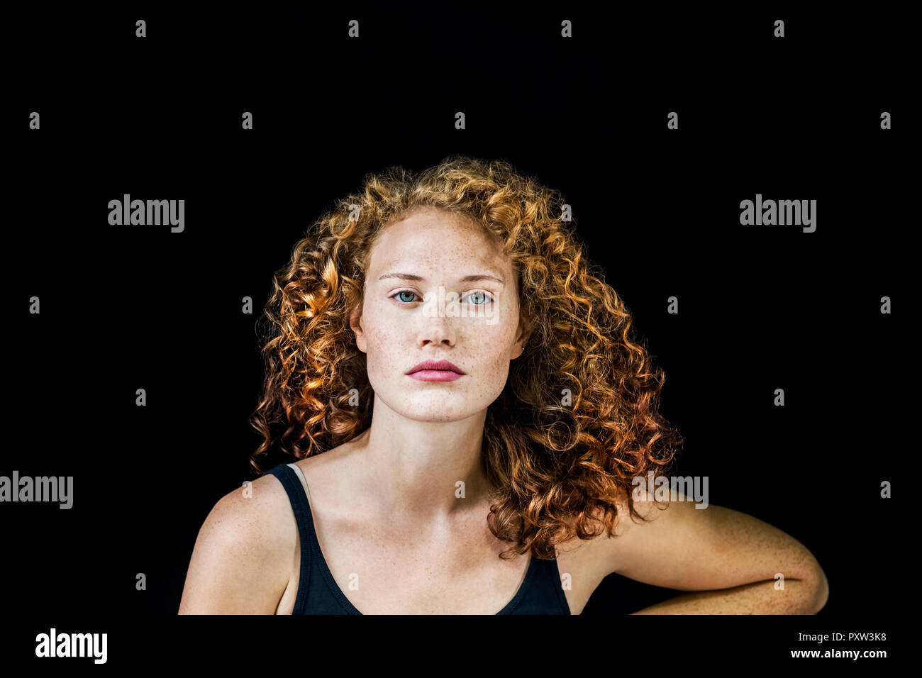 Ritratto di freckled giovane donna con ricci capelli rossi davanti a sfondo nero Foto Stock