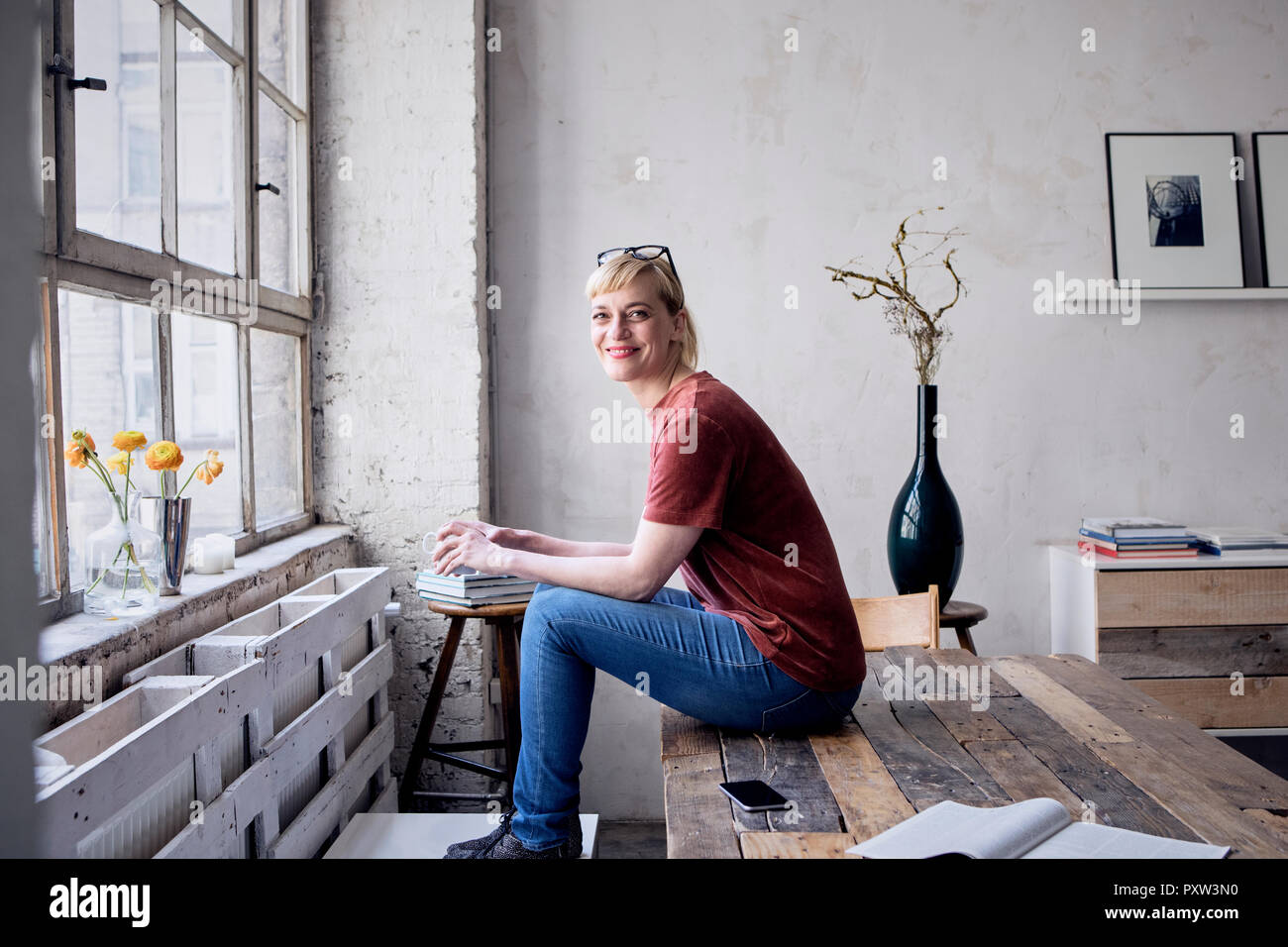 Ritratto di donna sorridente con tazza da caffè seduti sulla scrivania in mansarda Foto Stock