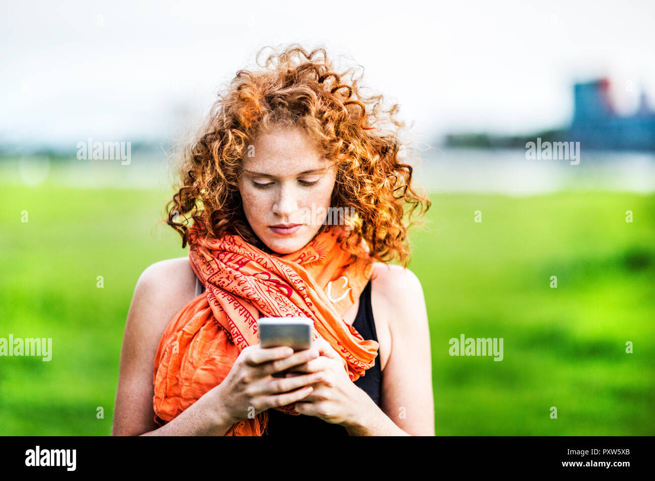 Ritratto di giovane donna con ricci capelli rossi guardando al telefono cellulare Foto Stock