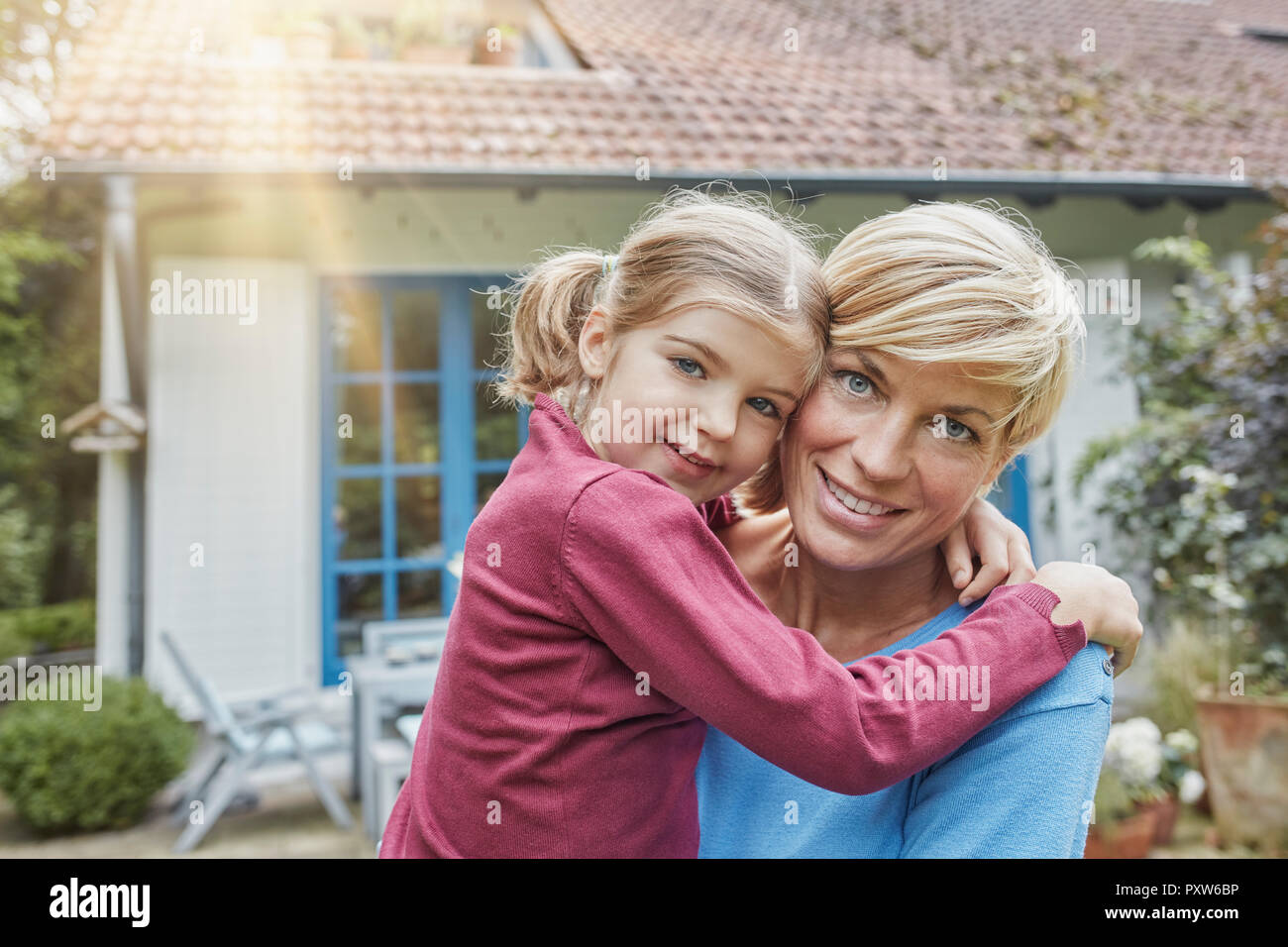 Ritratto di Madre sorridente portando la figlia davanti alla loro casa Foto Stock