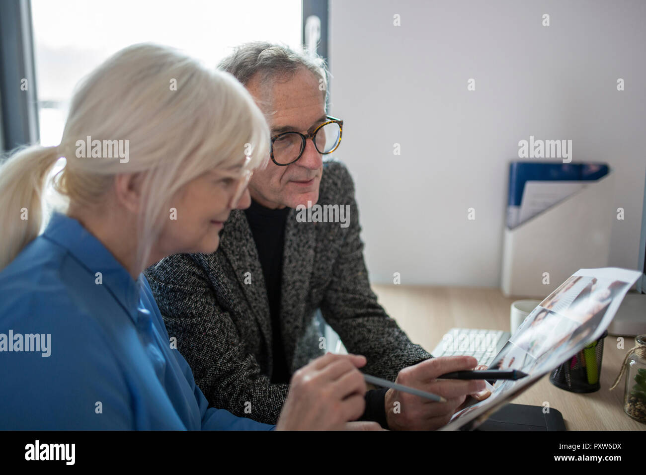 Due colleghi più anziani lavorando insieme alla scrivania in ufficio esaminando le foto Foto Stock