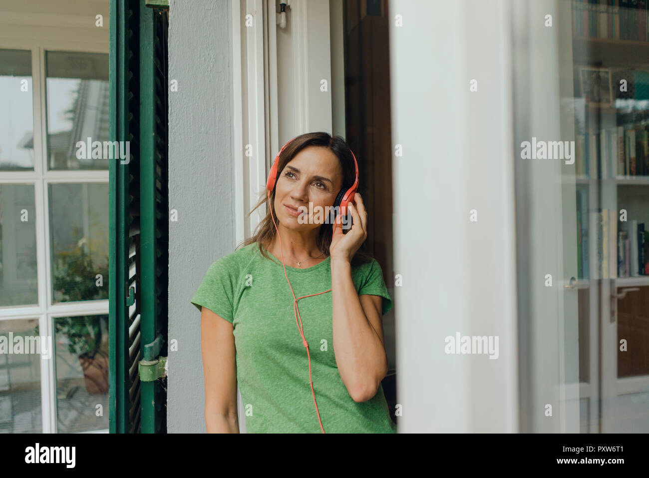 Donna matura in piedi alla terrazza porta in ascolto di musica con le cuffie Foto Stock