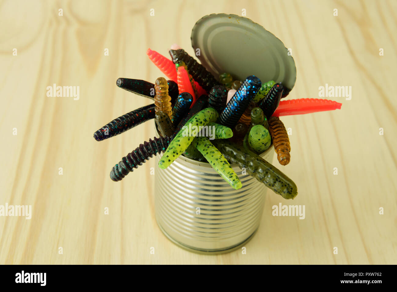 Close-up, Dettaglio, apertura può di worms, materia plastica artificiale worm-like creature strisciando fuori dello stagno su sfondo di legno, oggetti Foto Stock