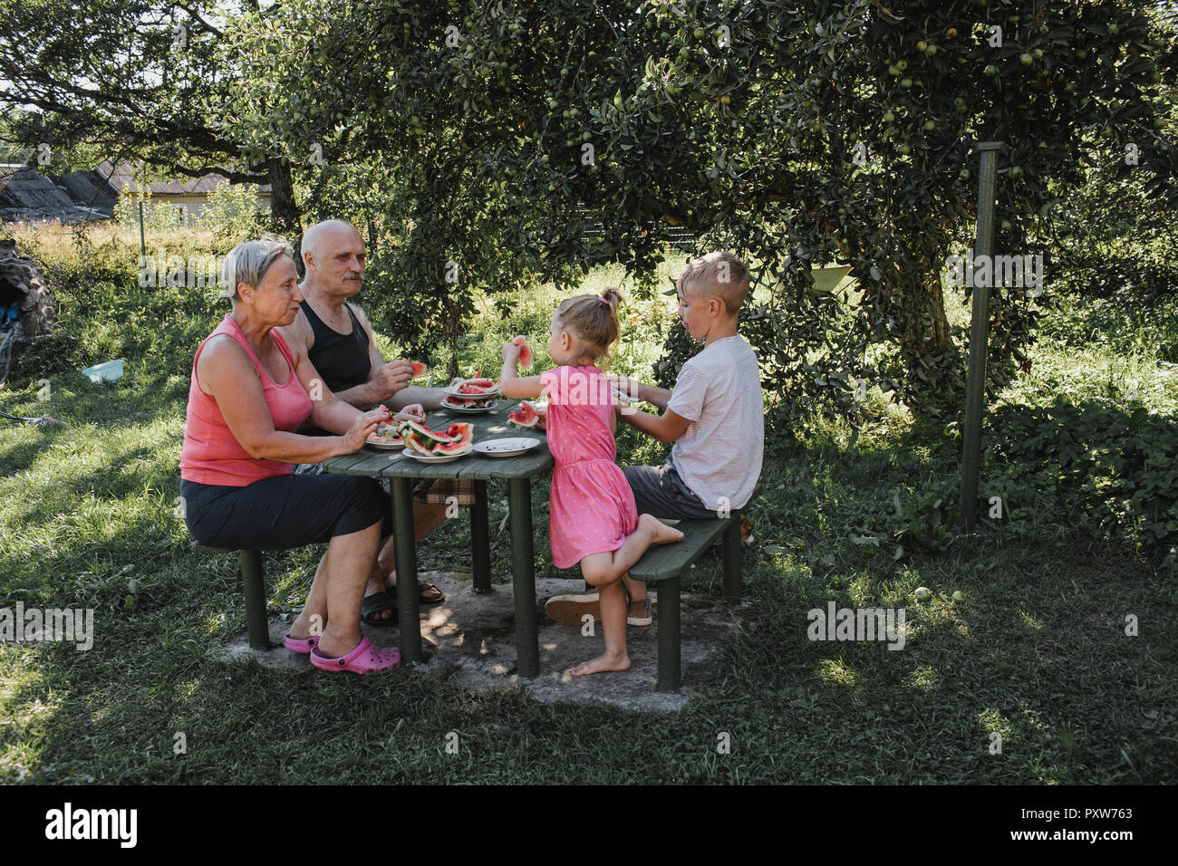 I nonni di trascorrere del tempo insieme con il nipote e nipote nel giardino mangiando anguria Foto Stock