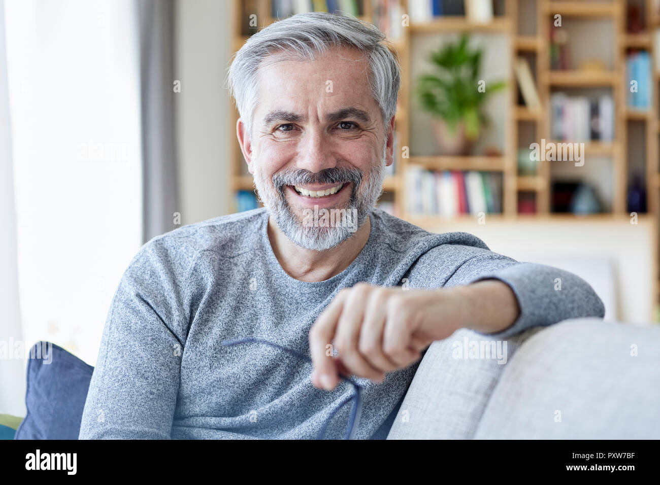 Ritratto di sorridere uomo maturo seduto sul divano di casa Foto Stock