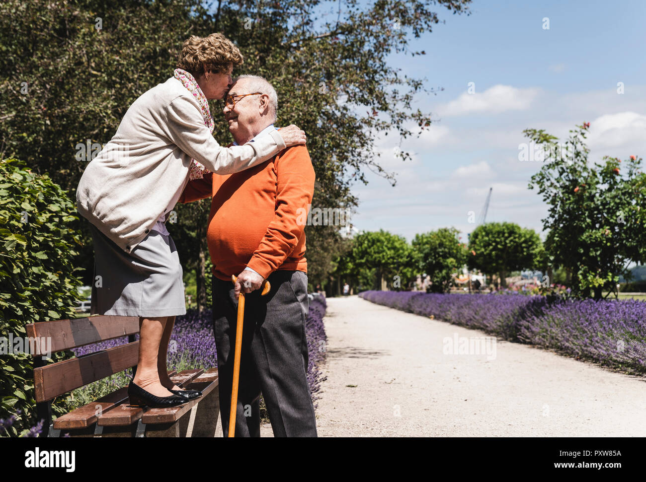 Coppia senior divertirsi nel parco, donna in piedi sul banco kissing senior uomo sul fronte Foto Stock