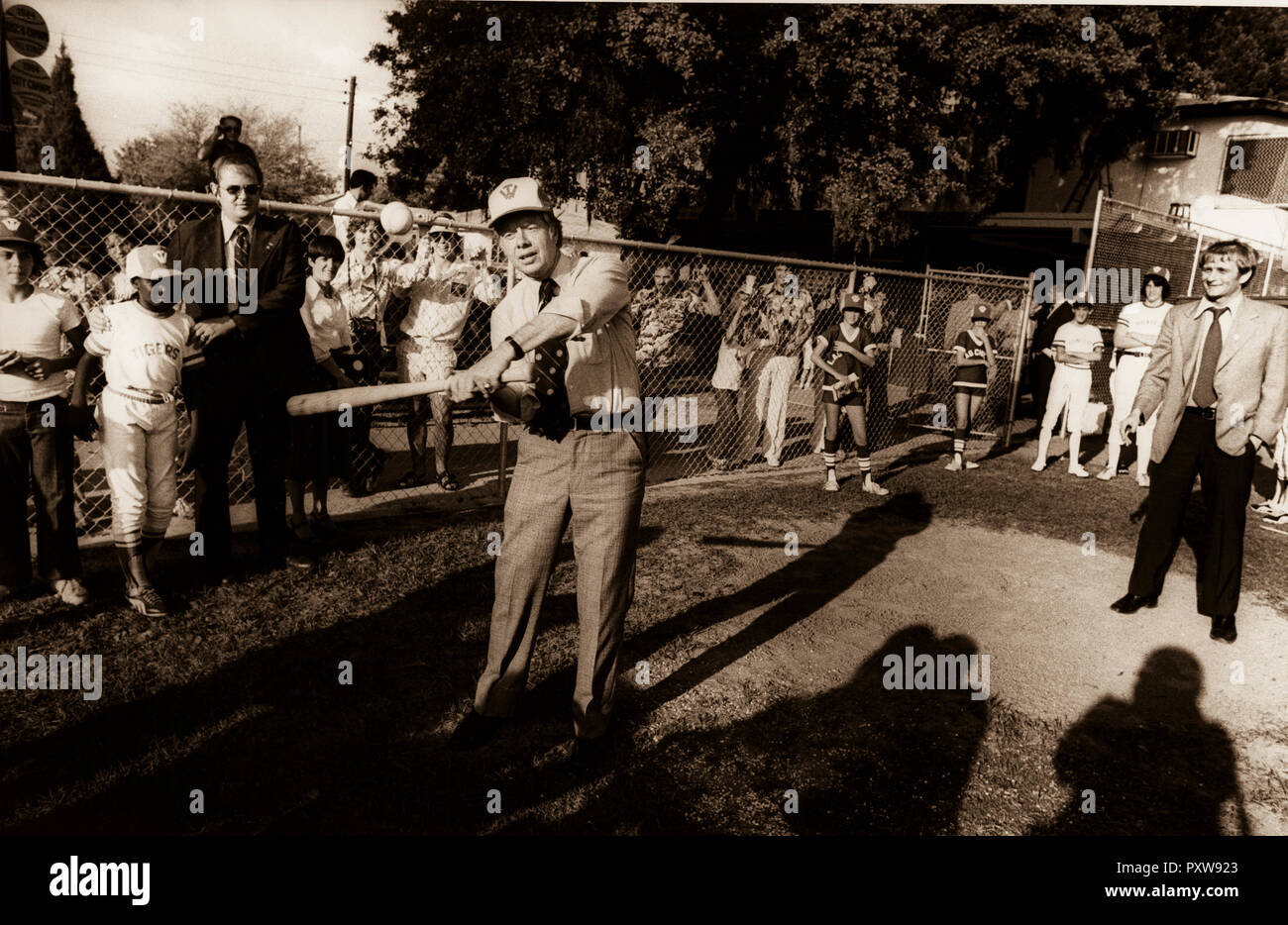 1976 Candidato presidenziale democratica Jimmy Carter si ferma la sua per il giro della Papamobile lungo il tragitto per un rally per visitare con i bambini delle elementari. Molti dei bambini Carter ha invitato ad unirsi a loro sul campo da baseball. Carter premere il segretario, Jody Powell è sulla destra e un servizio segreto USA agent contiene un ragazzo al di fuori del modo danneggia come Carter prende uno swing. Foto Stock