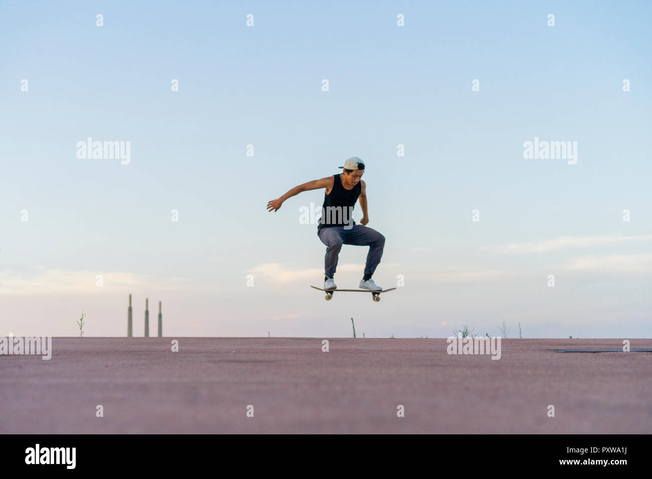 Giovane uomo facendo uno skateboard trick su una corsia al crepuscolo Foto Stock