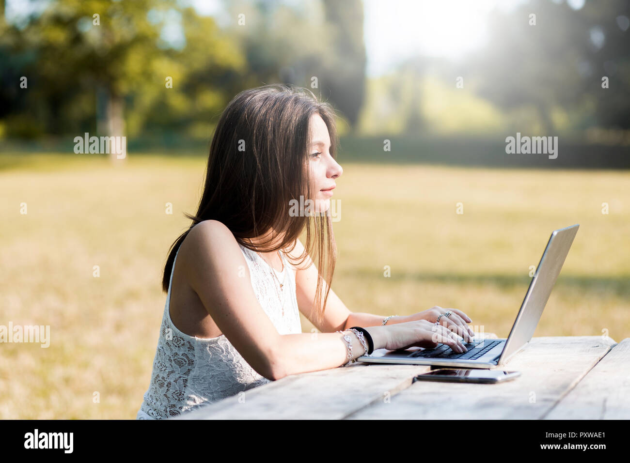 Giovane donna utilizzando computer portatile sul tavolo in legno all'esterno Foto Stock