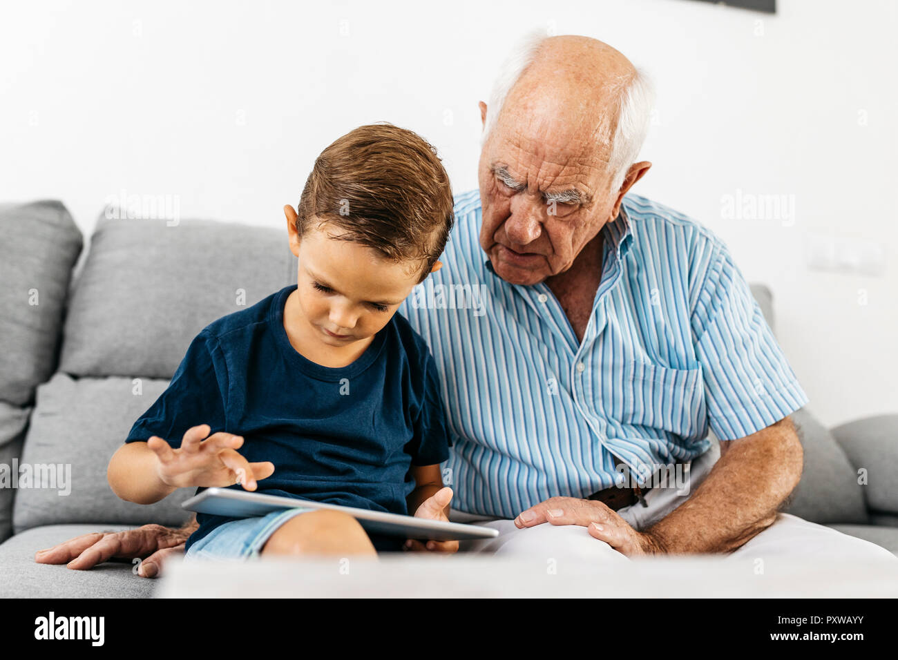 Nonno e nipote insieme seduti sul divano di casa utilizzando tavoletta digitale Foto Stock