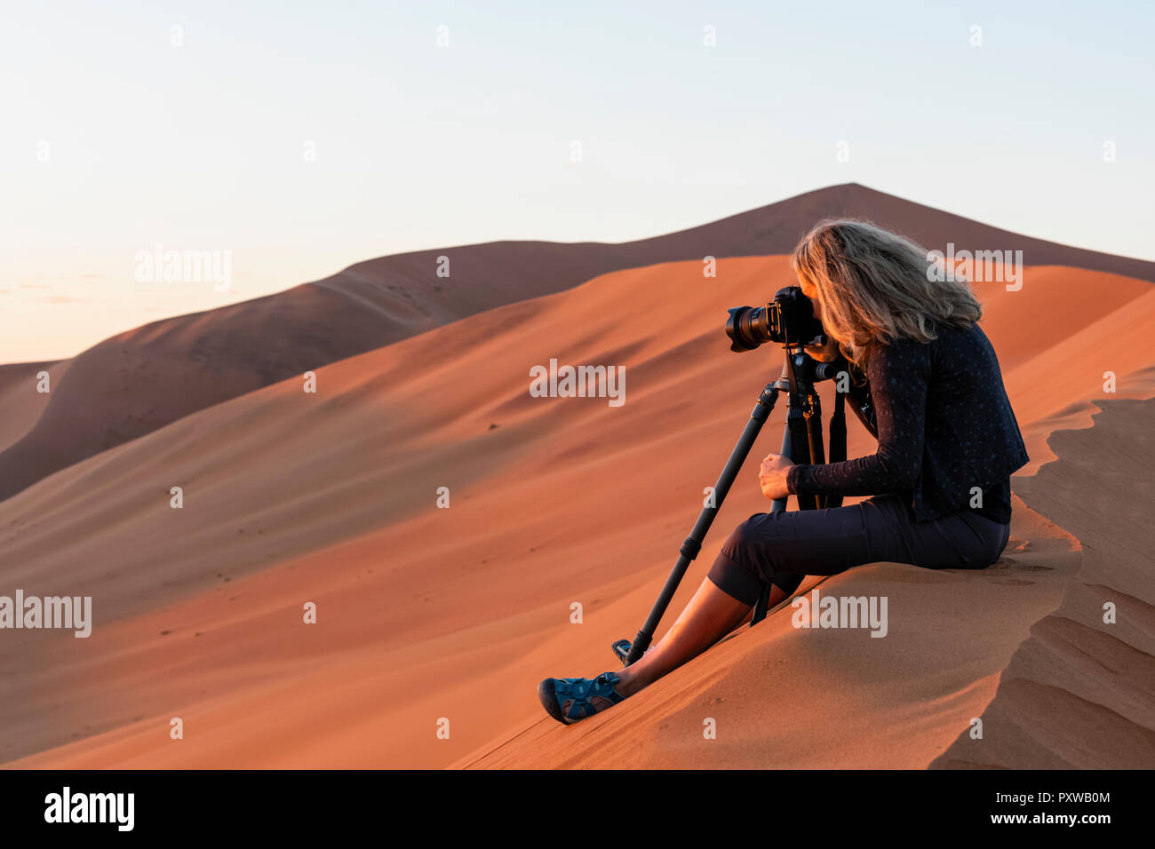 In Africa, la Namibia, il deserto del Namib Naukluft, Parco Nazionale, femmina photograper fotografare in Early Morning Light, seduti su una duna di sabbia Foto Stock