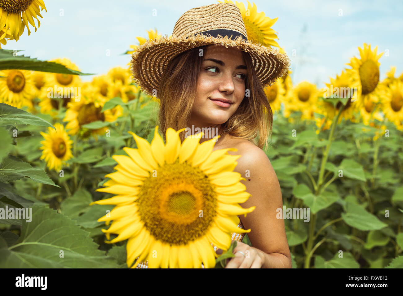 Giovane donna con un cappello di paglia sorridente in un campo di girasoli Foto Stock