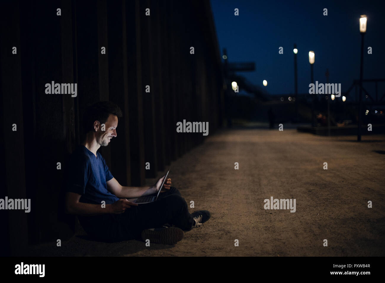 Metà uomo adulto seduto a gambe incrociate sulla terra, utilizzando computer portatile durante la notte Foto Stock