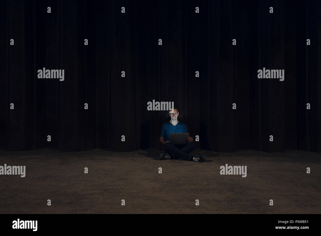 Metà uomo adulto seduto a gambe incrociate sulla terra, utilizzando computer portatile durante la notte Foto Stock
