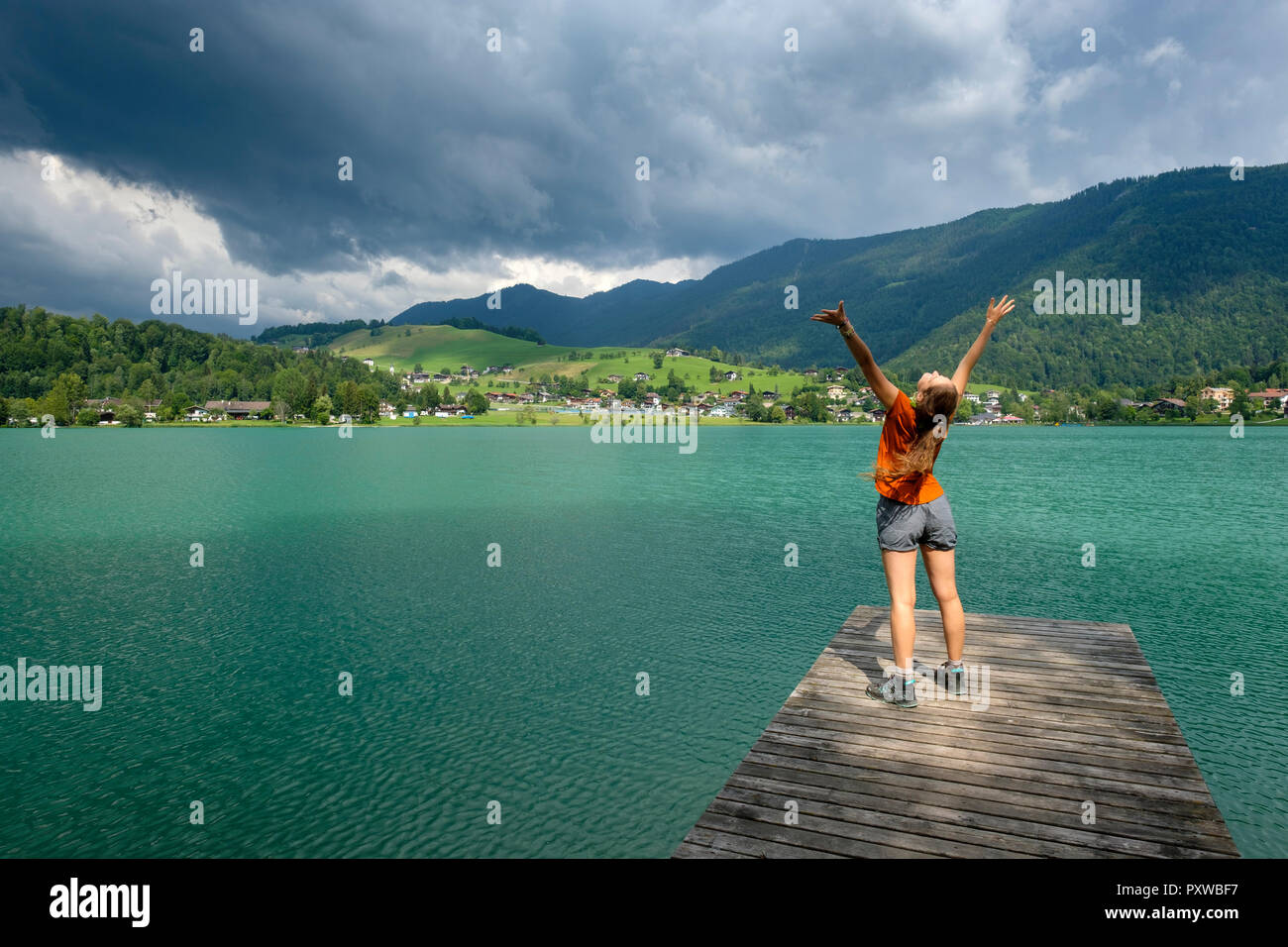 Adolescente in piedi sul molo in legno, bracci sollevati Foto Stock