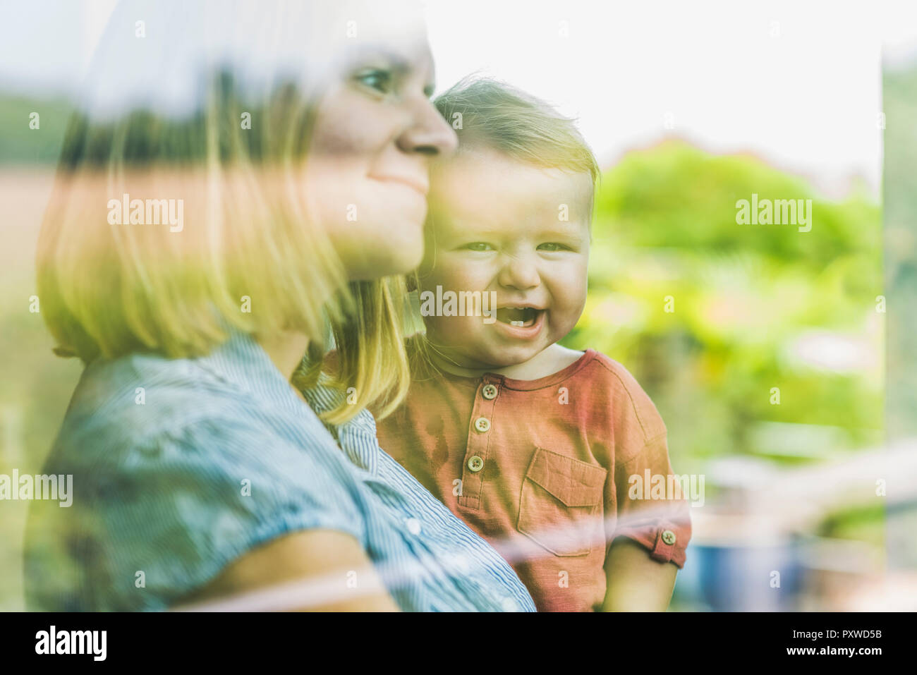 Madre guardando fuori della finestra, con il figlio sul suo braccio Foto Stock