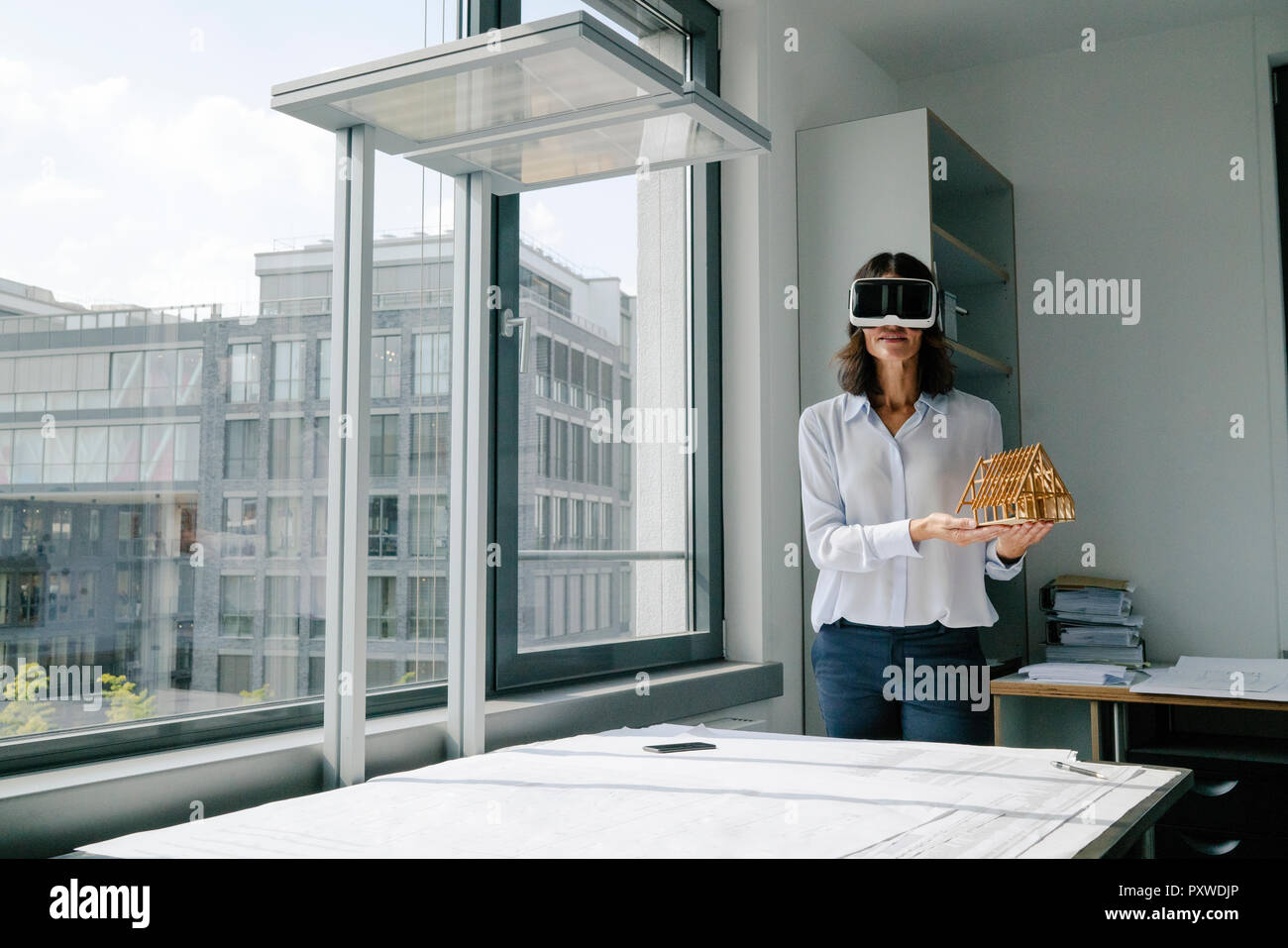 Donna che mantiene il modello architettonico della casa, utilizzando gli occhiali VR Foto Stock