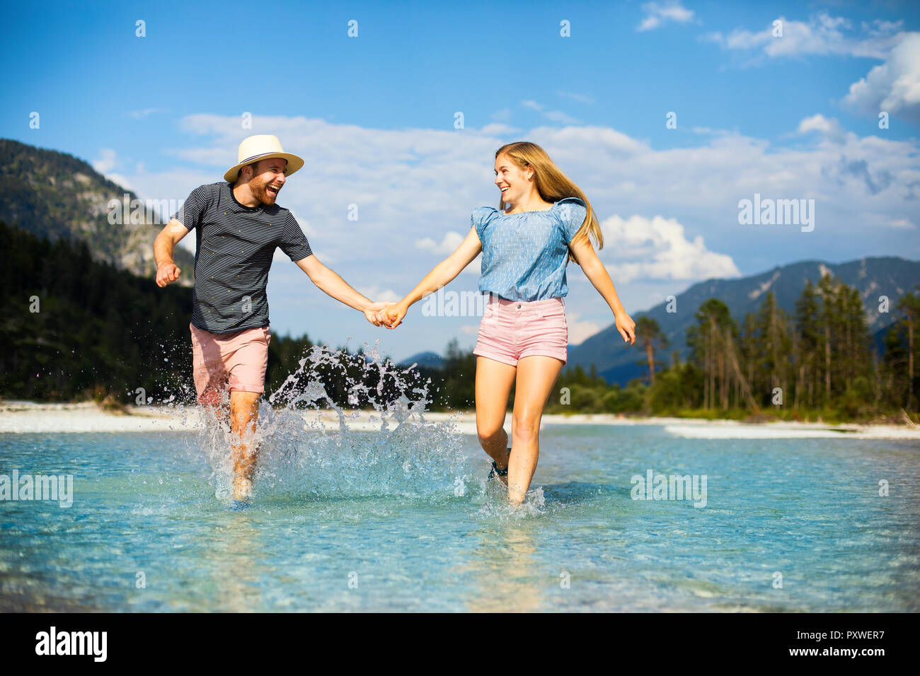 Coppia giovane tenendo le mani e in esecuzione attraverso l acqua Foto Stock