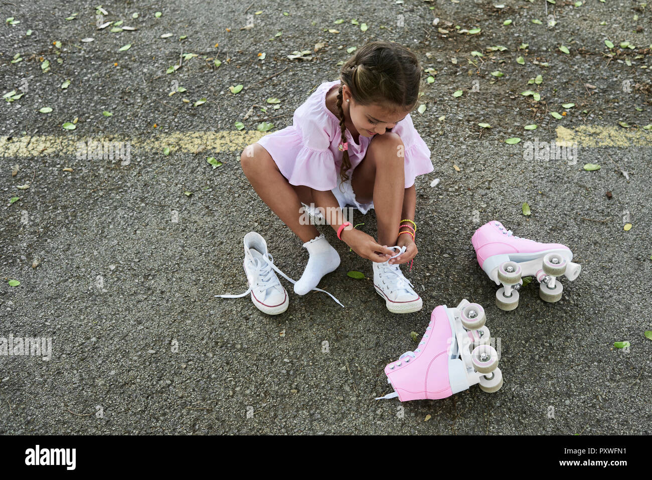 Bambina indossa camicetta rosa e trecce scarpe di legatura dopo il pattinaggio a rotelle Foto Stock