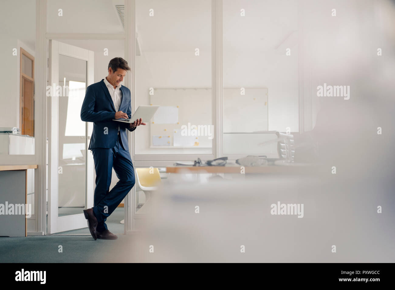 Imprenditore in piedi in ufficio, con il computer portatile Foto Stock