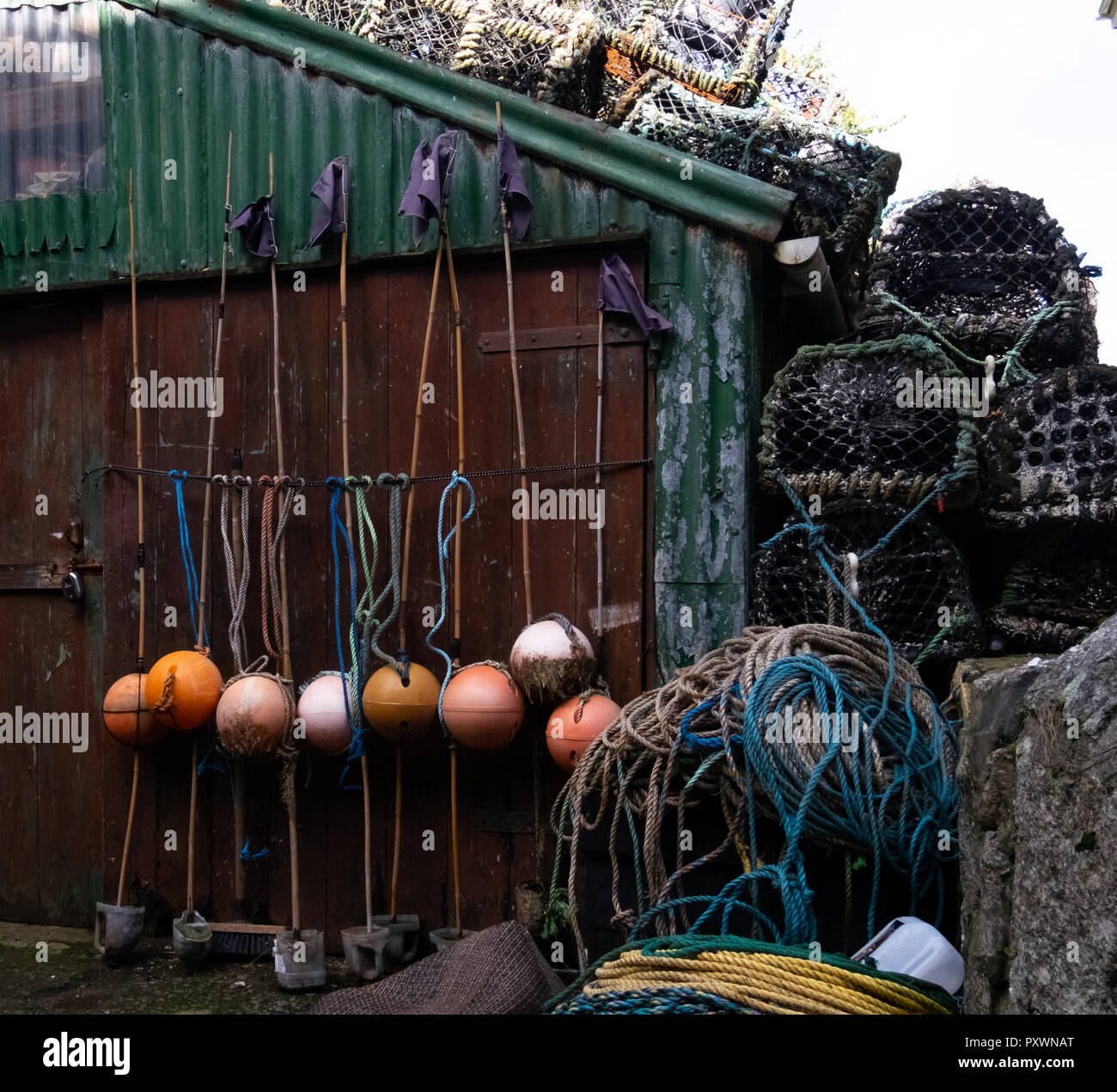 Diverse attività di pesca boe e una pila di aragosta pentole su un vecchio dipinto di verde ondulato capannone di stagno, cercando unkempt e senza tempo Foto Stock